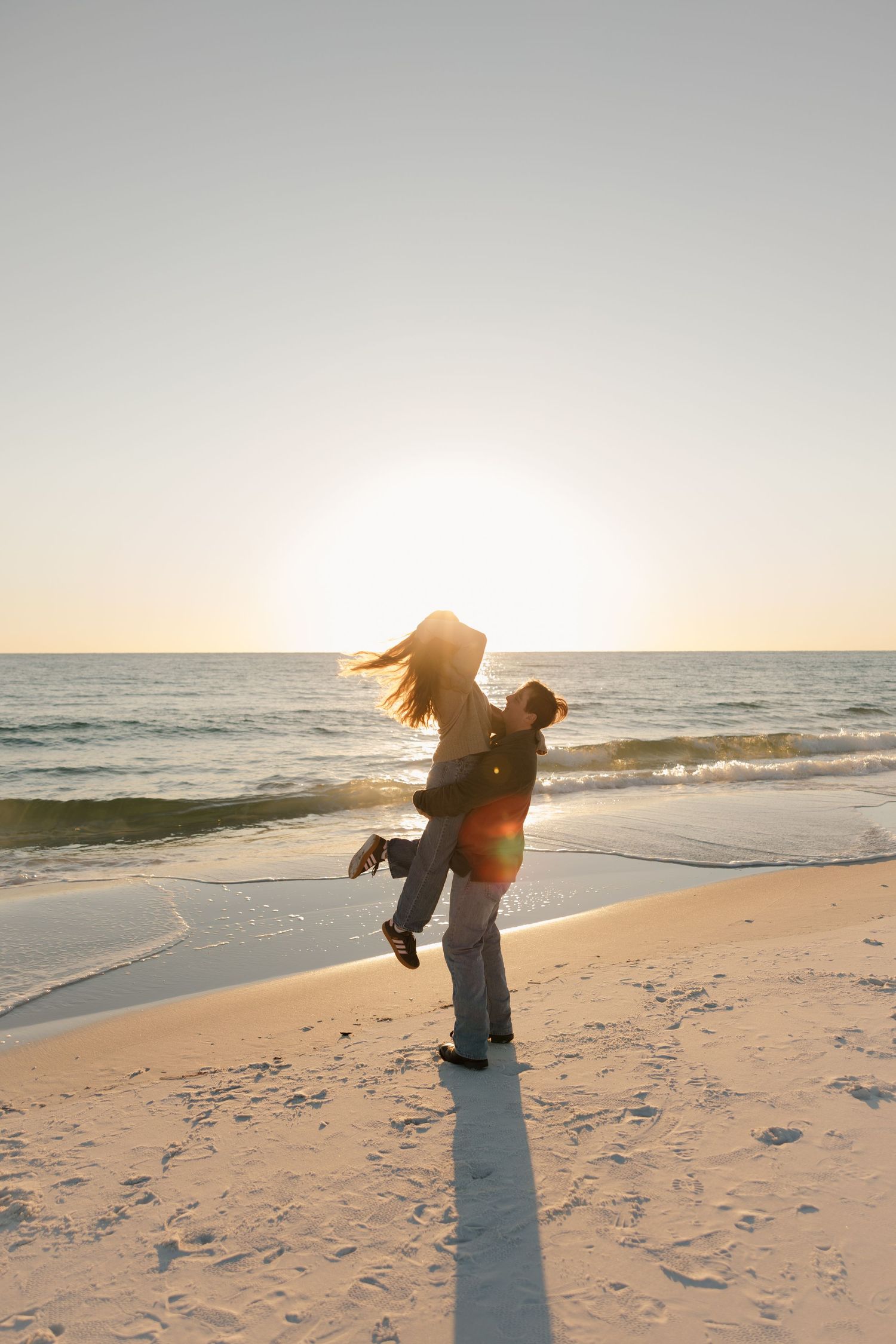 Couple in white clothing dancing together on beach under stormy sky.