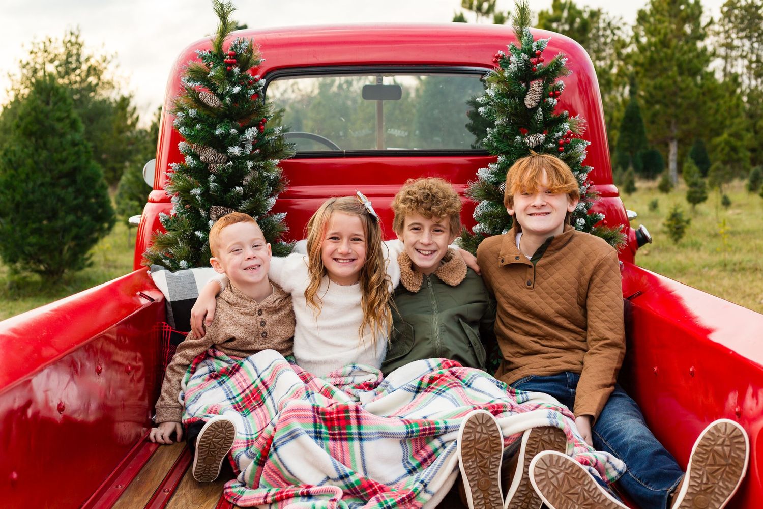 Smiling children in a red vintage truck decorated for Christmas mini sessions in Cedar Rapids, IA. Family photography by Nichole Sieck.