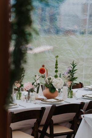 Elegant wedding reception table with floral centerpiece featuring orange dahlias, white hydrangeas, and greenery in a copper vase.