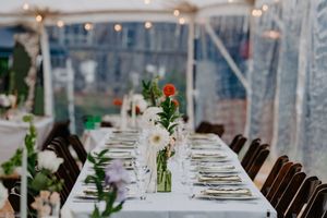 Elegant outdoor wedding reception table with white linens, floral centerpieces, and string lights under a clear tent.