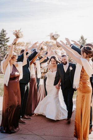 Bride and groom walk through an arch of raised arms formed by their wedding party outdoors.
