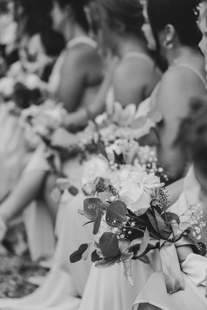 Black and white photo of bridesmaids holding floral bouquets with eucalyptus and white flowers at a wedding ceremony.