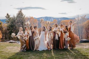 Bridesmaids in mismatched earth-tone dresses celebrate with bride against stunning autumn mountain backdrop.