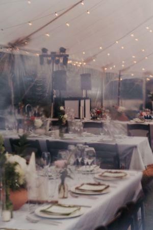 Romantic wedding reception under a clear tent with string lights, long tables set with white linens and glassware.