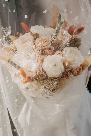 Elegant bridal bouquet featuring white ranunculus, blush roses, dried pampas grass, and baby's breath.