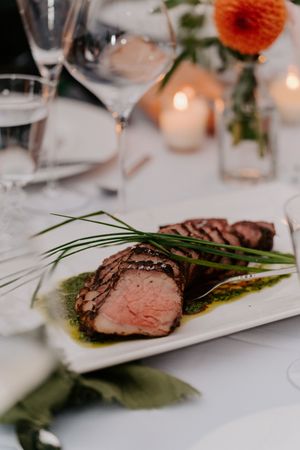 Sliced medium-rare steak garnished with fresh chives and herb sauce on a white plate at an elegant wedding reception dinner.