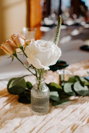 White and peach roses in a glass vase with eucalyptus greenery on a wedding reception table.