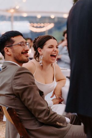 Bride and groom laughing joyfully at their wedding reception under string lights.