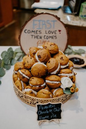 Pumpkin chocolate chip whoopie pies stacked on decorative gold stand at rustic wedding dessert table.