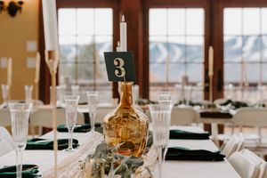 Wedding table centerpiece featuring amber glass vase, white taper candle, table number 3, and eucalyptus greenery.