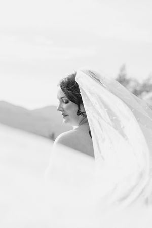 Black and white portrait of a bride with her veil flowing in the wind on her wedding day.