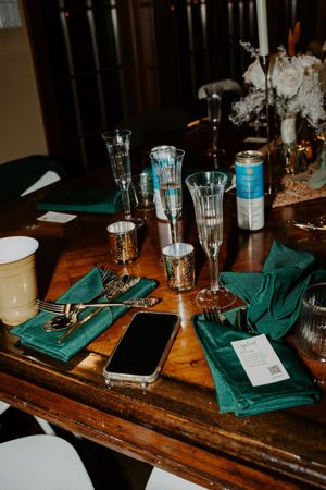 Elegant wedding reception table with green velvet napkins, crystal glasses, and gold cutlery.