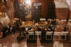 Overhead view of elegant wedding reception dinner tables with candles, greenery, and guests in a rustic venue.