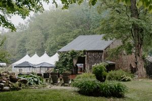Rustic barn venue with white event tents on lush green grounds surrounded by misty forested hills.