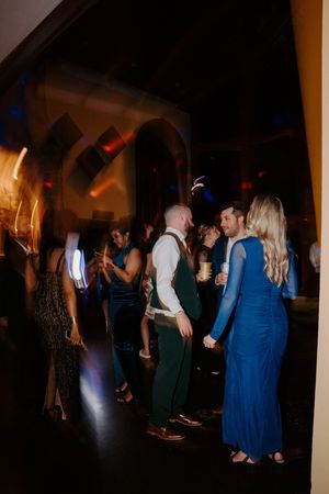 Wedding guests dance together under colorful lights at a lively indoor wedding reception celebration.