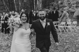 Joyful bride and bearded groom walking back down the aisle after their outdoor woodland wedding ceremony.