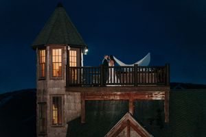 Romantic couple shares kiss on illuminated tower balcony against deep blue night sky at wedding.
