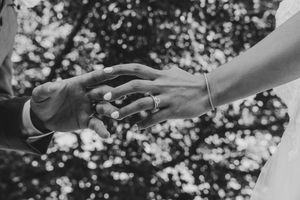 Black and white wedding photo of couple holding hands, showing engagement ring and bracelet with bokeh background.