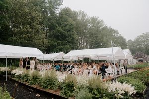 Elegant outdoor wedding ceremony under white tents surrounded by lush greenery and garden flowers.