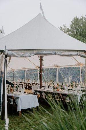 Elegant outdoor wedding reception under white sailcloth tent with long tables and floral centerpieces.