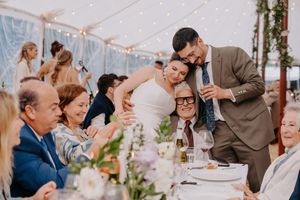 Bride and groom share a tender moment with elderly guest at elegant tented wedding reception dinner.