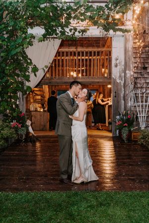 Bride and groom share romantic first dance kiss outside rustic barn wedding venue.