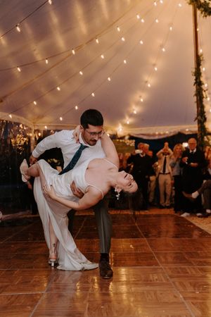 Bride and groom share romantic first dance dip under warm string lights at elegant tented wedding reception.