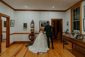 Bride and groom share a first look moment in a rustic museum venue with hardwood floors and nautical decor.