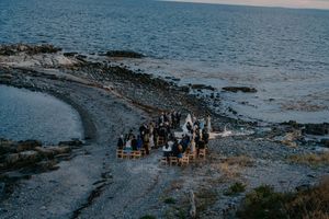 Aerial view of an intimate outdoor wedding ceremony on a rocky coastal shoreline at dusk.