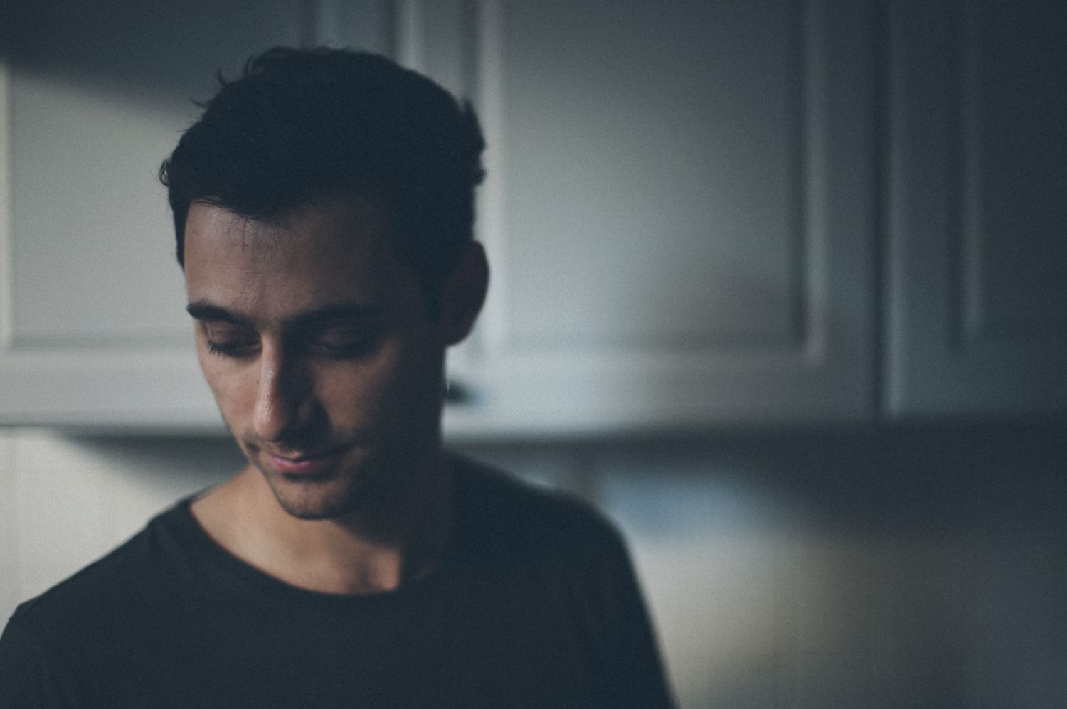 Moody low-key portrait of person in black shirt looking downward in dramatic lighting.