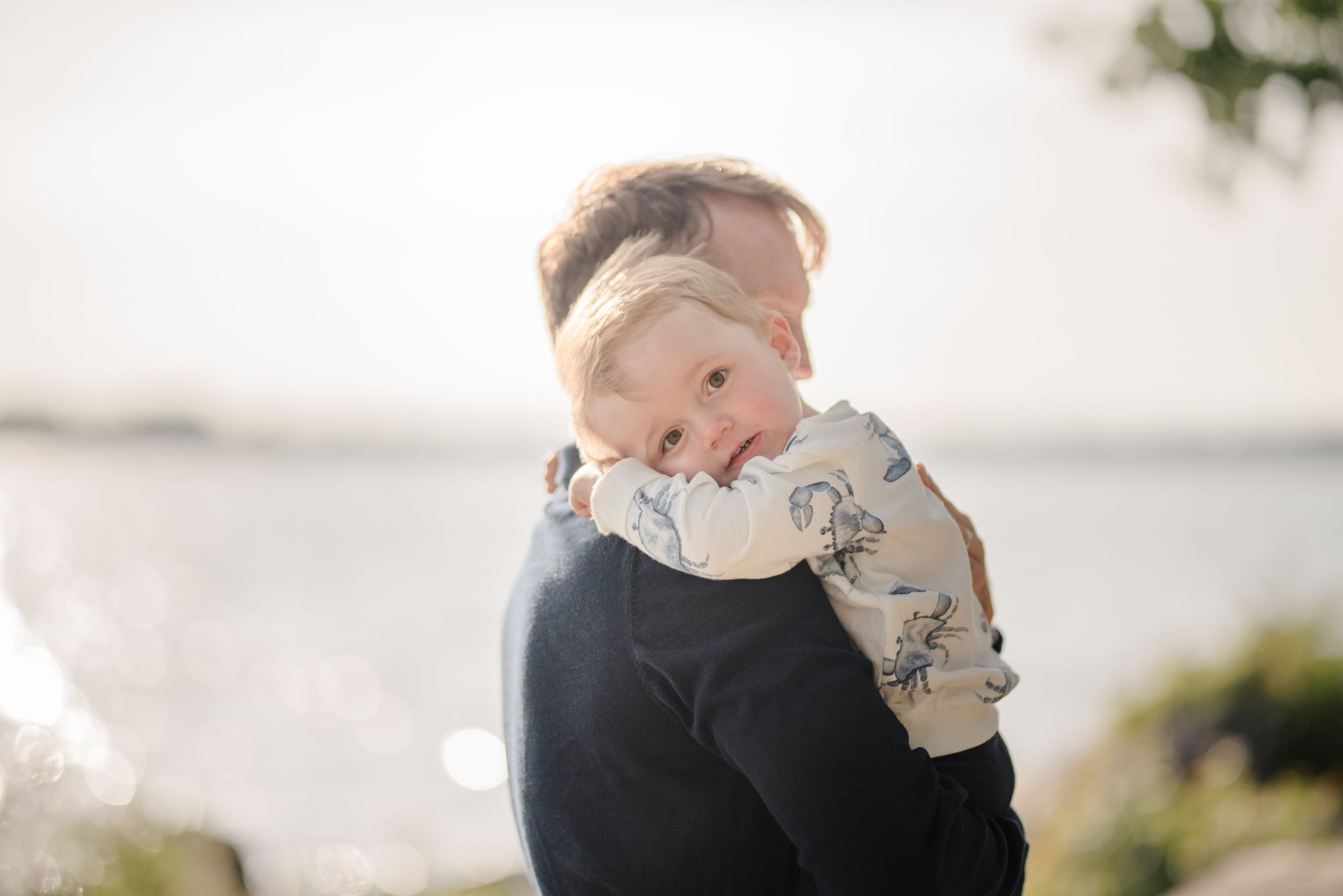 Family shares tender embrace against bright sunlit background.