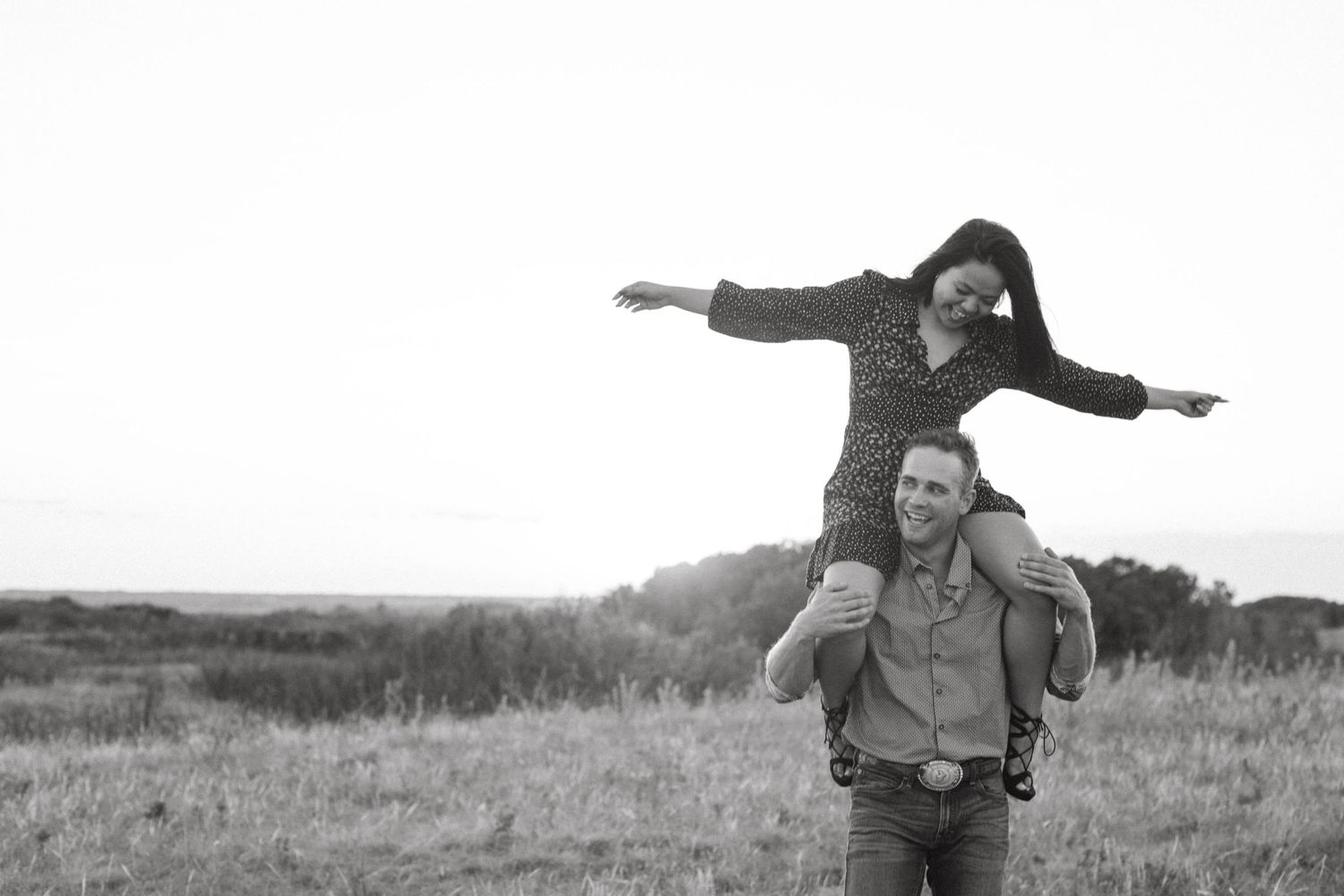 A playful couple enjoys a piggyback ride in a scenic field at sunset.