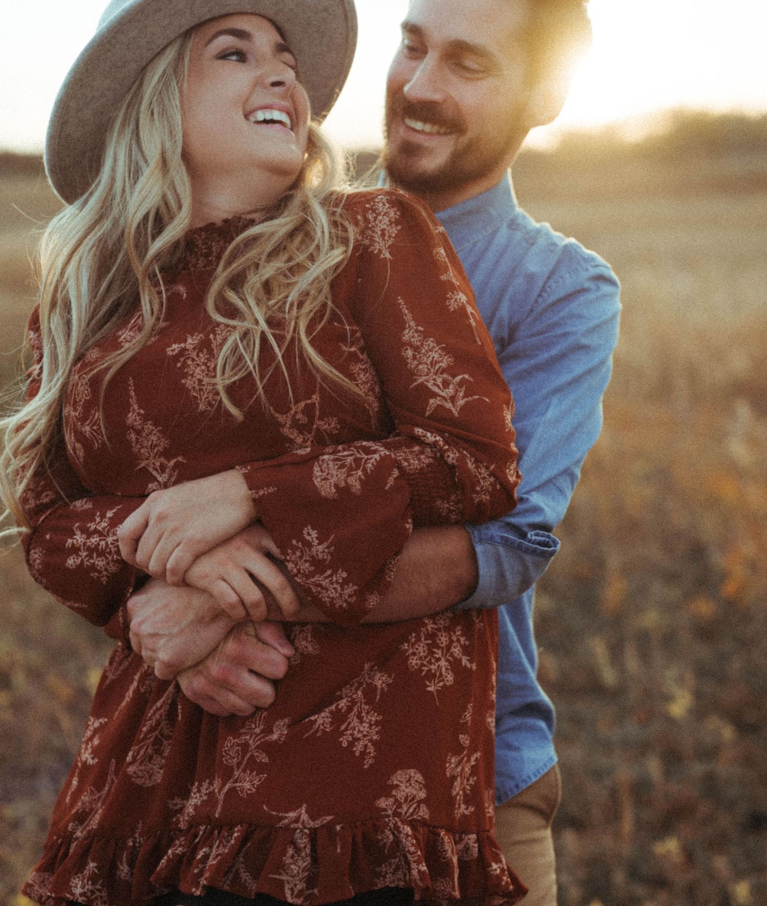 Romantic couple embracing in a sun-lit field during golden hour.