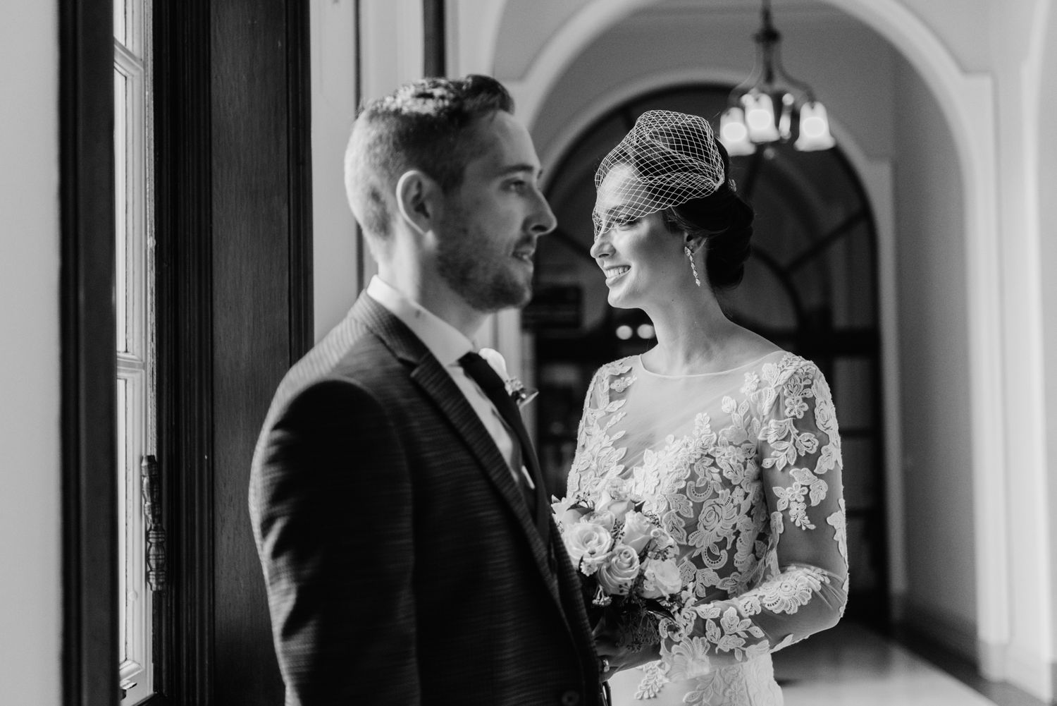 Black and white photo of a couple in wedding attire posing in a corridor