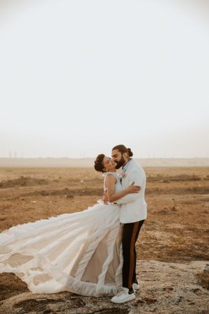 A romantic wedding couple embraces on a hilltop overlooking a desert landscape.