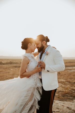 A tender moment between newlyweds backlit by golden sunlight in a desert setting.