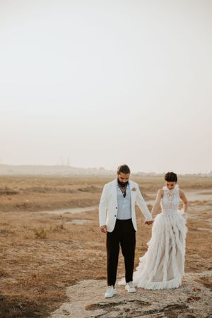 A wedding couple walks hand in hand along a desert path at sunset.