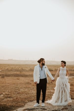 A couple poses in formal wedding attire on a desert landscape at golden hour.