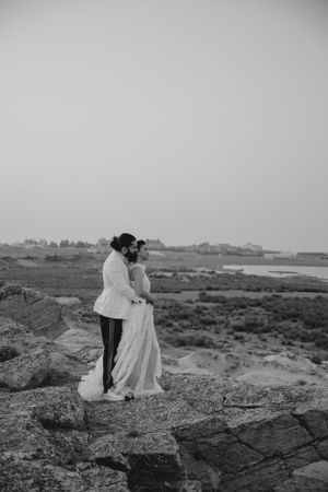 A black and white photo of newlyweds standing on rocky coastal cliffs.