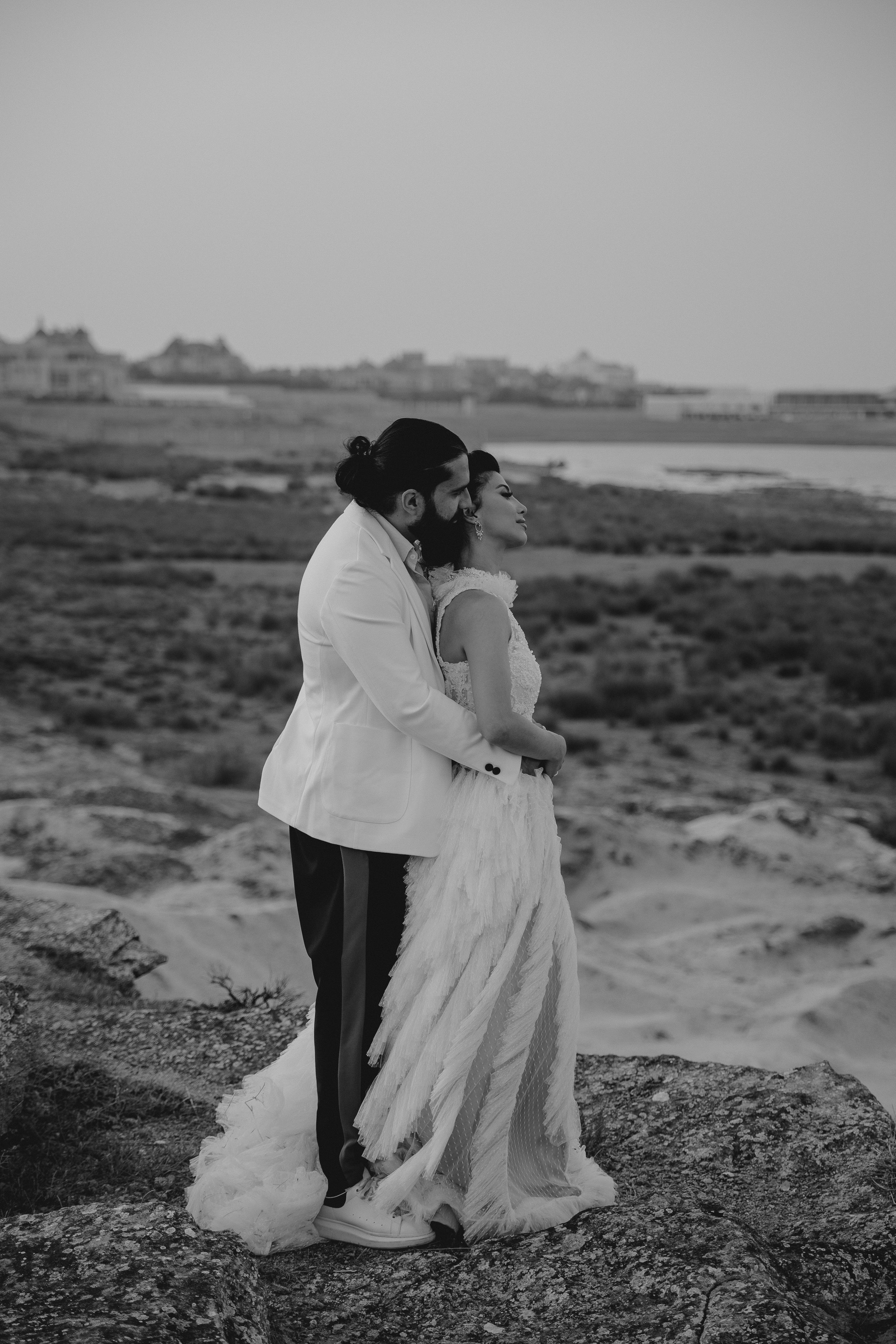 A black and white portrait of newlyweds overlooking a coastal landscape.