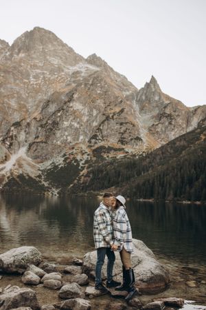 Two people in matching plaid jackets share a moment against a mountainous backdrop.