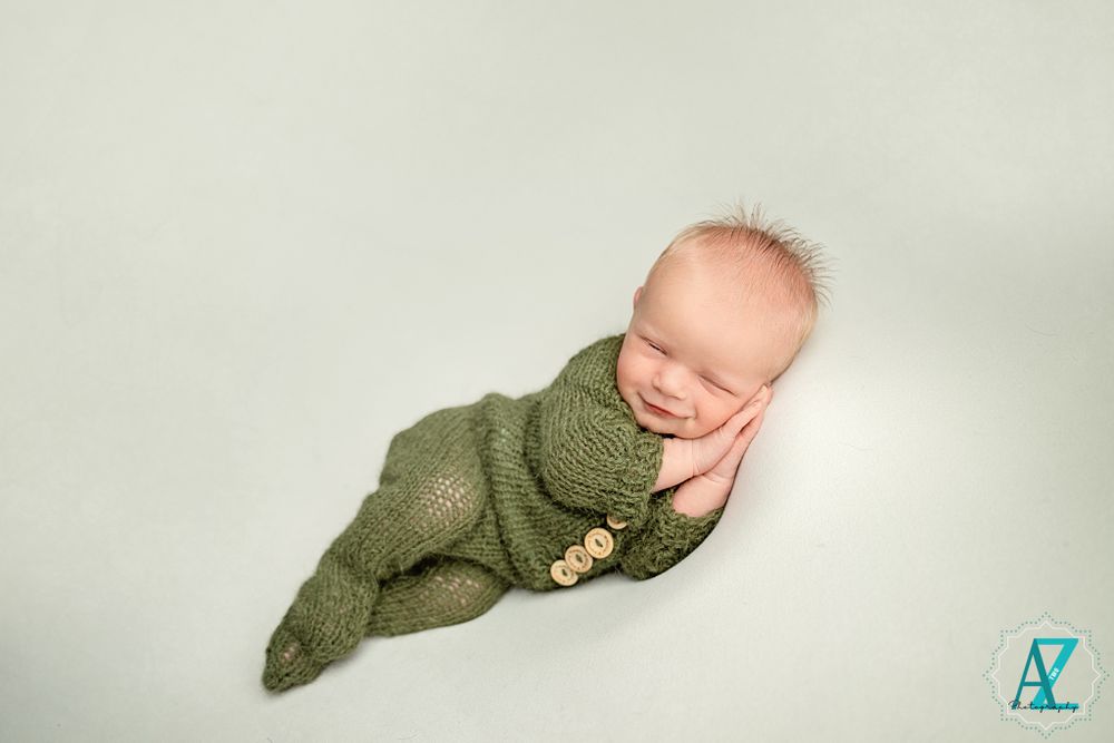 Sleeping newborn wrapped in sage green knit outfit against white background.