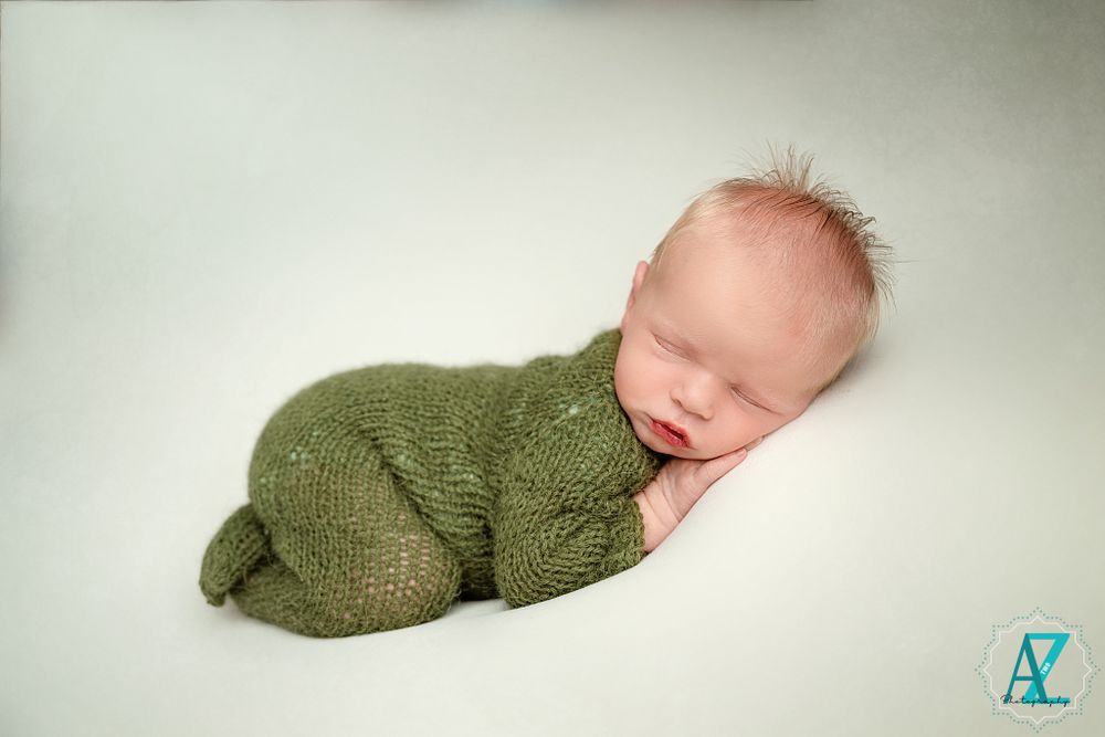 Sleeping infant wearing cozy green knitted outfit on white background.