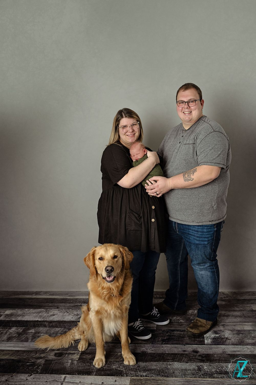 Casual family studio portrait with friendly golden retriever on wooden floor.
