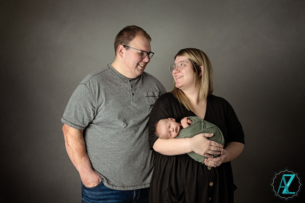 A couple smiles lovingly while holding their newborn baby in a professional studio portrait.