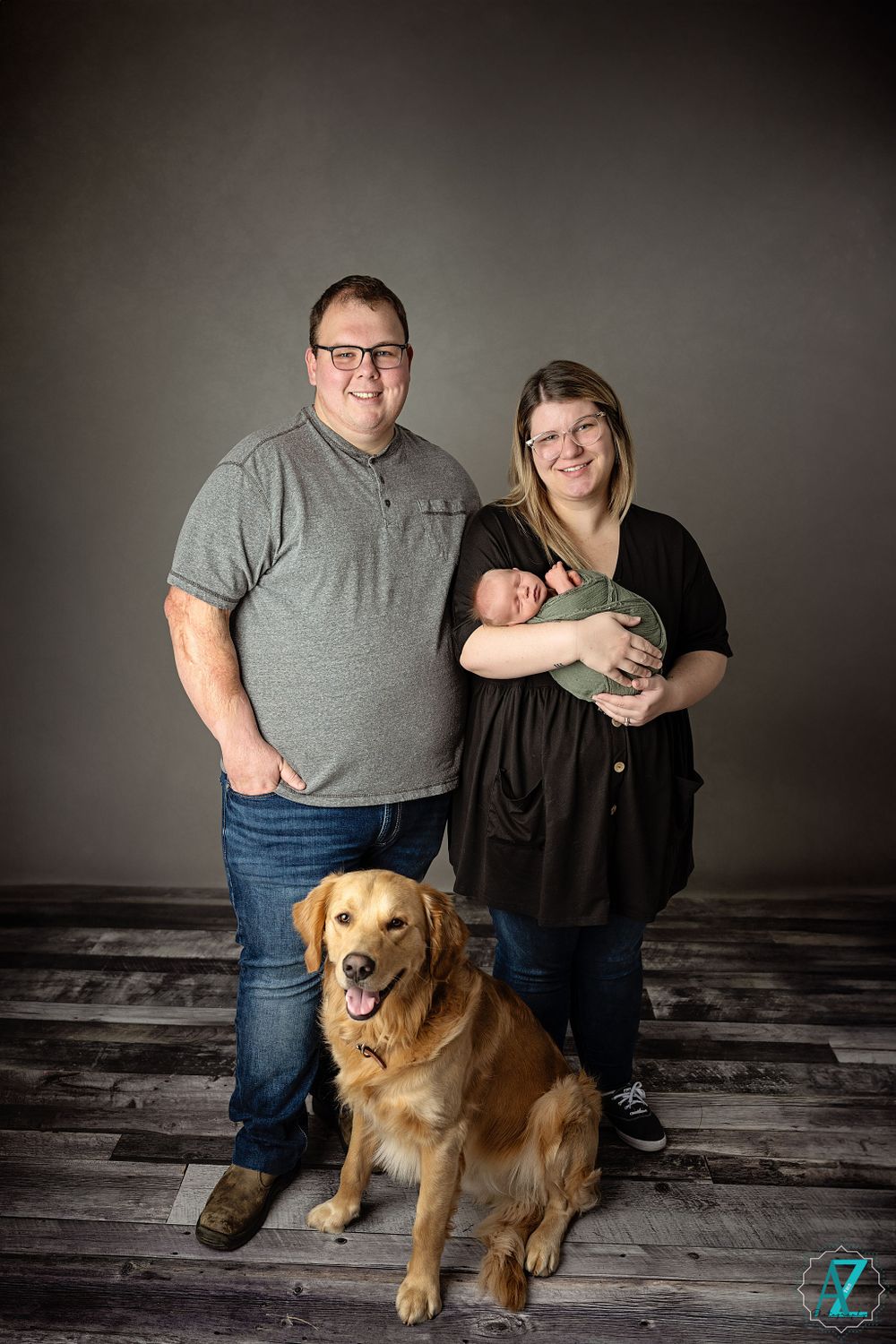 Family portrait with a golden retriever dog and newborn baby in a studio setting.