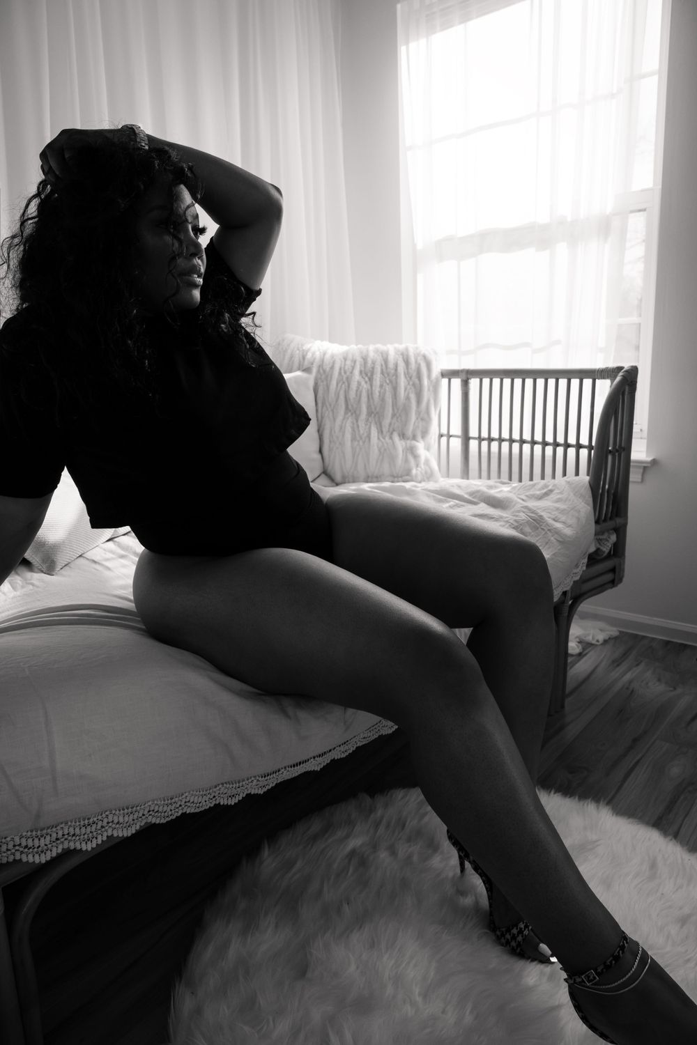Monochrome boudoir photo with soft window lighting and lace curtains.