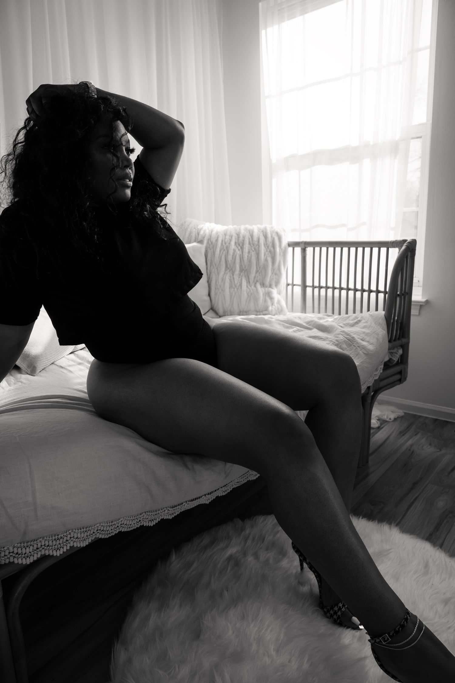 Monochrome boudoir photo with soft window lighting and lace curtains.