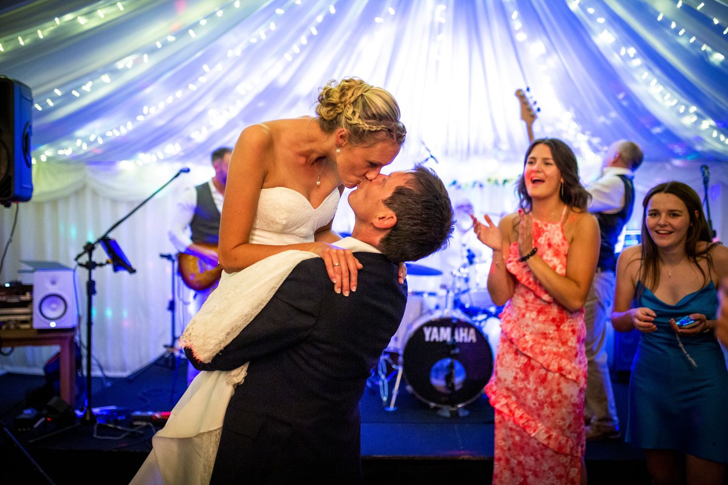 Wedding celebration with guests dancing under blue and white tent lighting.