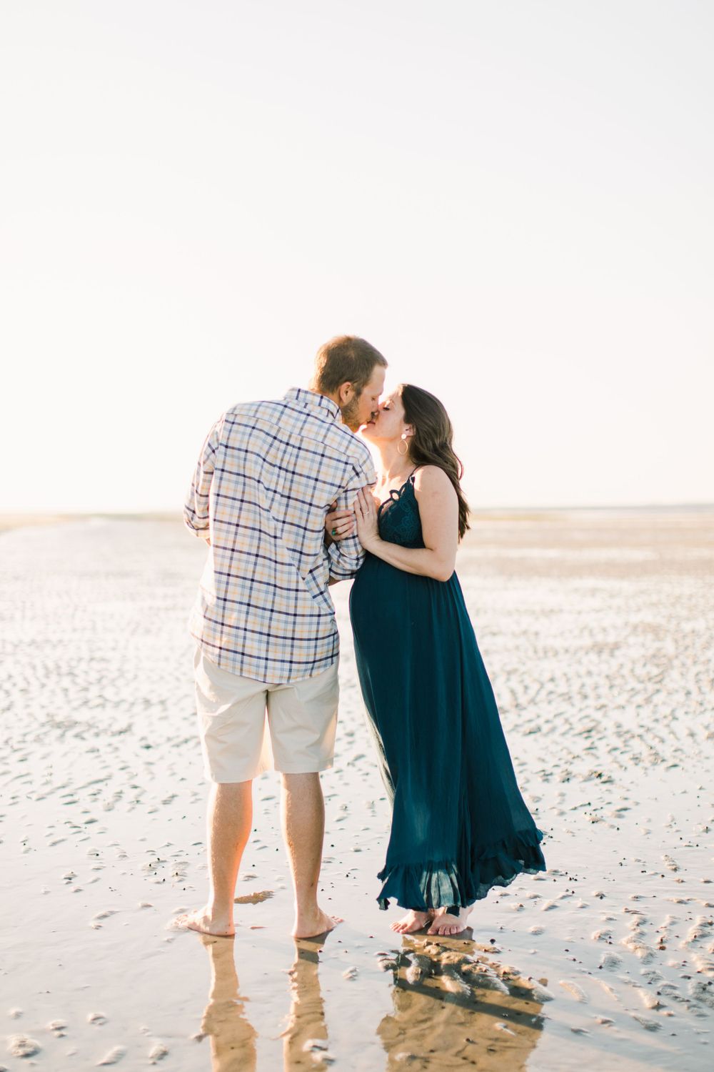 A couple sharing an intimate moment on a wet sandy beach at sunset.